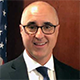 Nicholas Betty smiling wearing glasses, suit and tie.