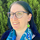 Siobhan Goldberg smiling, wearing glasses and a blue scarf.